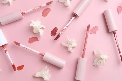 Different lip glosses, applicators and flowers on pink background, flat lay Stock Photos