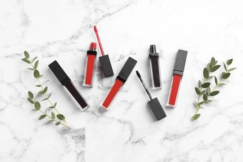 Different lip glosses, applicators and green leaves on white marble table, .. Stock Photos