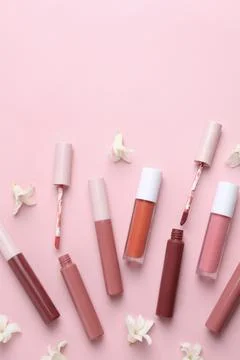 Different lip glosses, applicators and flowers on pink background, flat lay Stock Photos