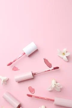 Different lip glosses, applicators and flowers on pink background, flat lay.. Stock Photos