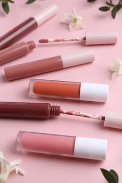 Different lip glosses, applicators, flowers and green leaves on pink backgrou Stock Photos