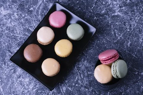 Different macarons of different flavors on a black plate. Stock Photos
