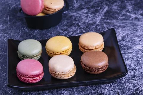 Different macarons of different flavors on a black plate. Fotos Stock