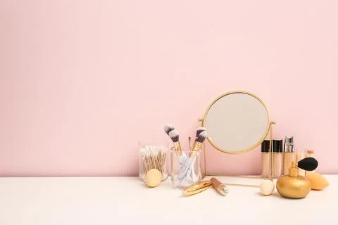 Different makeup products with mirror and hairbrush on white table against pi Stock Photos