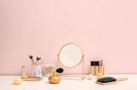 Different makeup products with mirror and hairbrush on white table against pi Stock Photos
