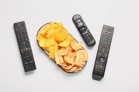 Different modern TV remote controls and plate with potato chips on grey backg Stock Photos