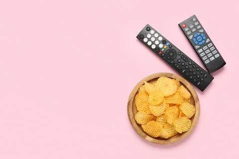 Different modern TV remote controls and board with potato chips on pink backg Stock Photos