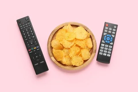 Different modern TV remote controls and board with potato chips on pink backg Stock Photos