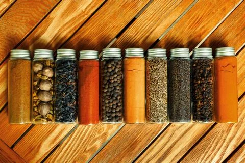Different multi-colored indian spices in transparent jars lie on a wooden Stock Photos