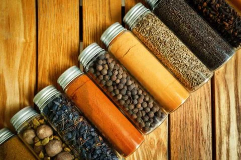Different multi-colored spices in transparent jars lie on a wooden background Stock Photos
