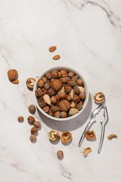 Different nuts in a white plate with a nutcracker on a gray table Stock Photos