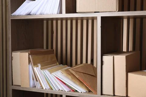 Different paper envelopes and parcels on wooden shelves in post office 스톡 사진
