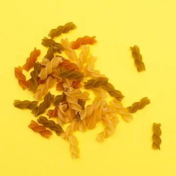 Different pasta in the form of spirals of brown, yellow and green colors on y Stock Photos