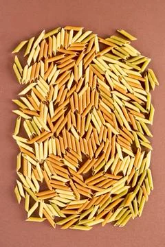 Different pasta in the form of tubes of brown, yellow and green colors Stock Photos