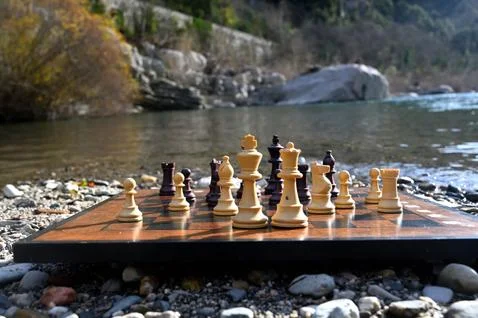 Different pieces on a chess board in front of the river Stock Photos
