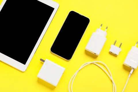 Different power adapters, blank mobile phone and tablet computer on yellow ba Stock Photos
