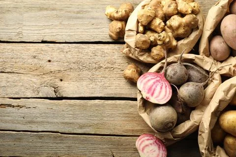 Different raw root vegetables in paper bags on wooden table, flat lay. Spac.. Stock Photos