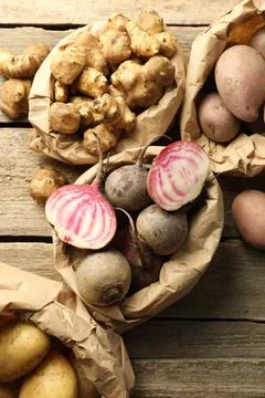 Different raw root vegetables in paper bags on wooden table, flat lay Stock Photos