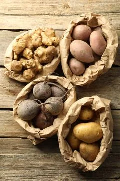 Different raw root vegetables in paper bags on wooden table, flat lay Stock Photos