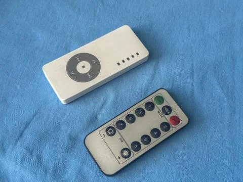 Different remote controls on blue fabric surface in bright light Stock Photos