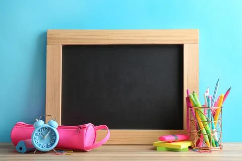 Different school stationery and small blank chalkboard on table near light bl Stock Photos
