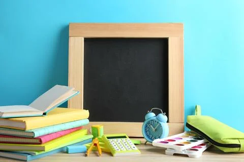 Different school stationery and small blank chalkboard on table near light bl Stock Photos