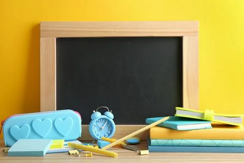 Different school stationery and small blank chalkboard on table near yellow w Stock Photos