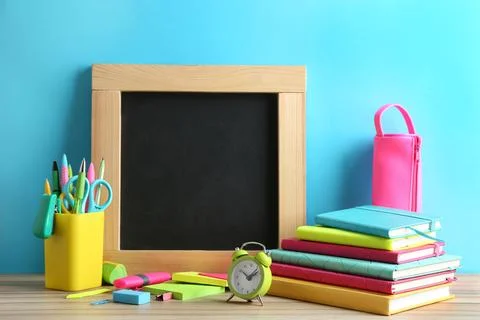 Different school stationery and small blank chalkboard on table near light bl Stock Photos