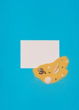 Different sea shells on bright yellow sand with white paper card note on blue Stock Photos