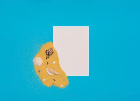 Different sea shells on bright yellow sand with white paper card note on blue Stock Photos