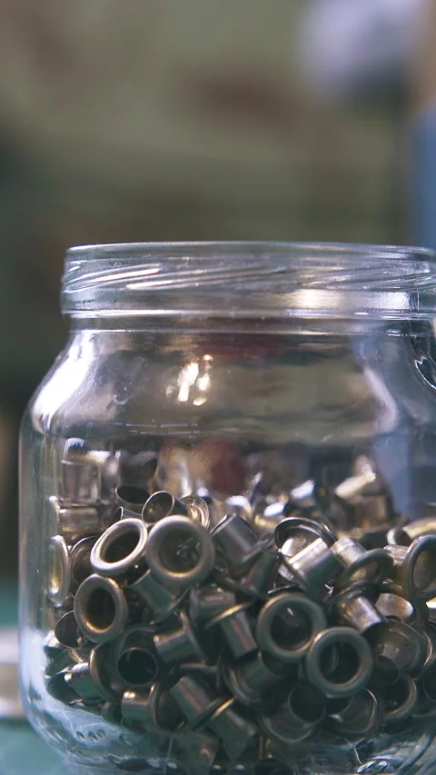 Different silver eyelet parts lie in transparent jar closeup Stock Footage 317100333
