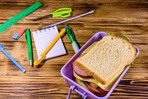 Different stationeries and lunch box with sandwiches on a wooden table Фото