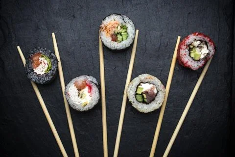Different sushi rolls on a black background with chopsticks Stock Photos