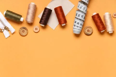 Different thread spools with buttons, measuring tape and zipper on orange bac 写真素材