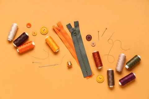 Different thread spools with buttons, pins and zippers on orange background 写真素材