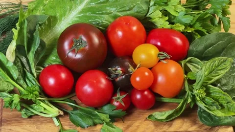 Different tomatoes among the various fresh greens on cutting board Stock Footage 347977086