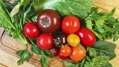 Different tomatoes among the various fresh greens on cutting board Stock Footage 347977155