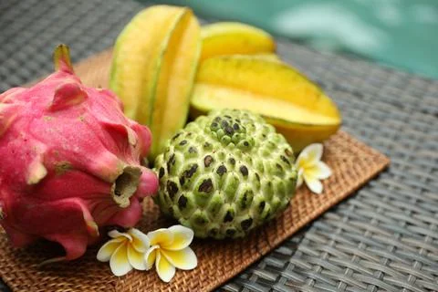 Different tropical fruit on wicker table near swimming pool, closeup Stock Photos