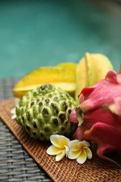 Different tropical fruit on wicker table near swimming pool, closeup. Space.. Stock Photos