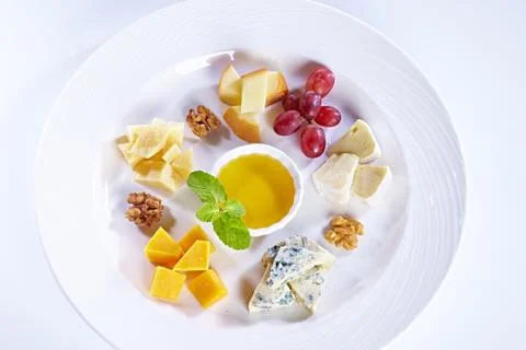 Different type of cheese with honey, grape, nuts on white plate. Top view. Blue Stock Photos