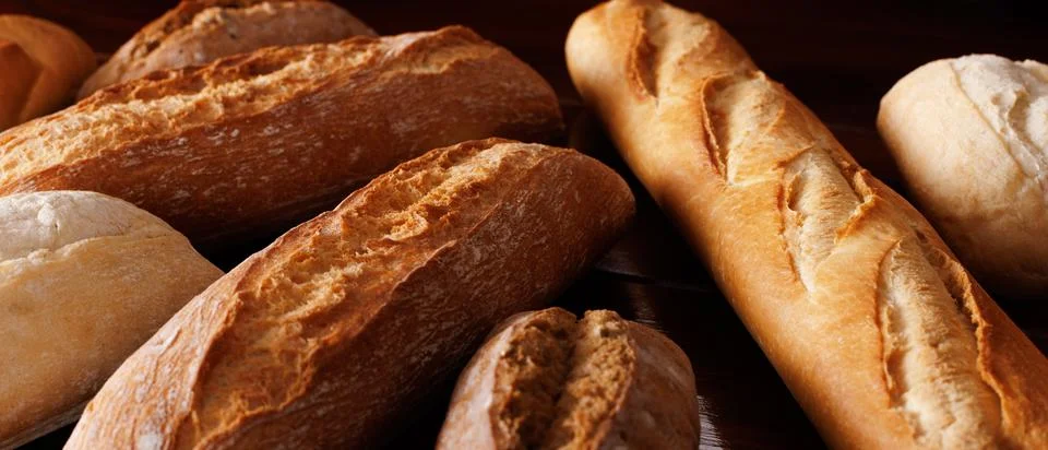 Different types of baked bread lie on a dark wooden table. Angle view. Select Stock Photos
