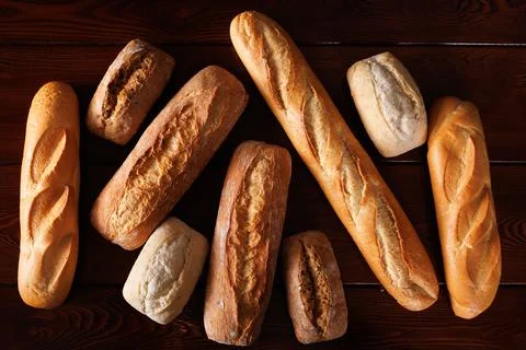 Different types of baked bread lie on a dark wooden table. View from above. Stock Photos