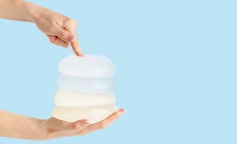 Different types of breast implants in hands on blue background. Copy space Stock Photos