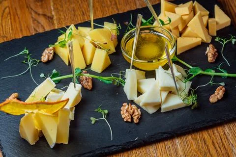 Different types of cheese on a black board with honey and nuts Stock Photos