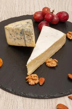 Different types of cheese on a black graphite board with dried apricots, walnuts Stock Photos