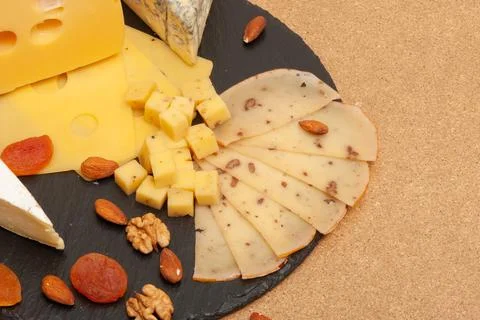Different types of cheese on a black graphite board with dried apricots, walnuts Stock Photos
