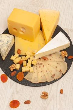 Different types of cheese on a black graphite board with dried apricots, walnuts Stock Photos