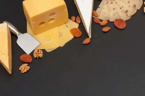 Different types of cheese on a black graphite board with dried apricots, walnuts Stock Photos