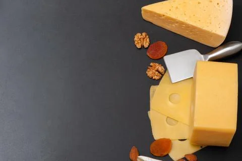 Different types of cheese on a black graphite board with dried apricots, walnuts Stock Photos