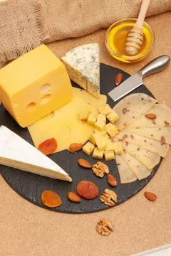 Different types of cheese on a black graphite board with dried apricots, walnuts Stock Photos